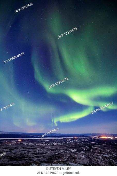 The aurora borealis glows over the Delta River and the distant lights of Fort Greely and Delta Junction, Interior Alaska, USA
