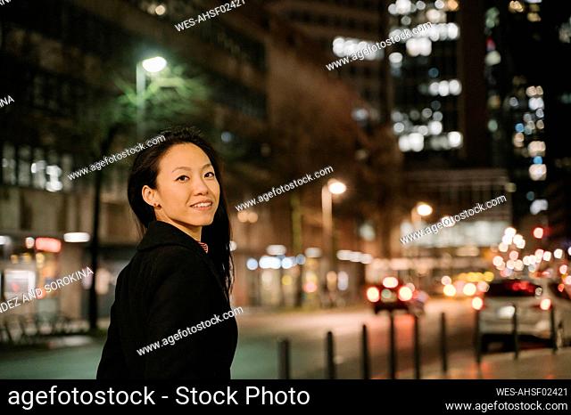 Portrait of a confident young woman in the city at night, Frankfurt, Germany