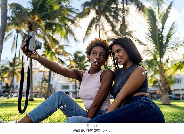 Two happy female friends taking an instant photo in a park