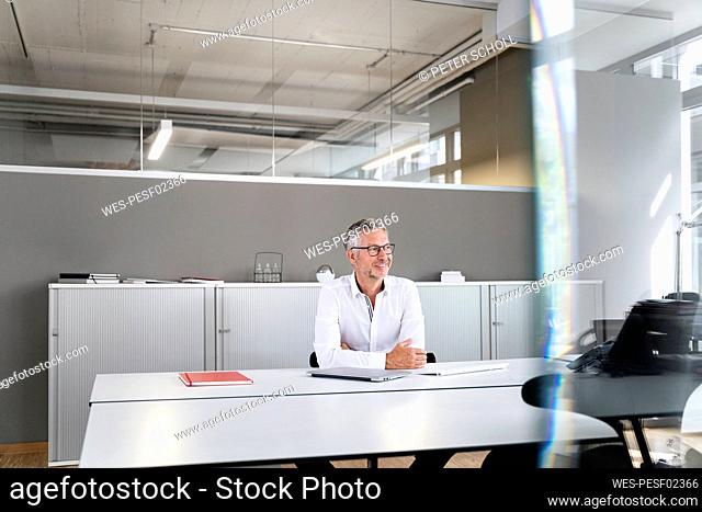 Thoughtful male entrepreneur looking away while leaning on desk in office