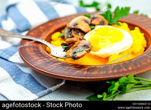 Traditional Italian polenta with mushrooms and a fork in a ceramic plate on a table with linen cloth, selective focus