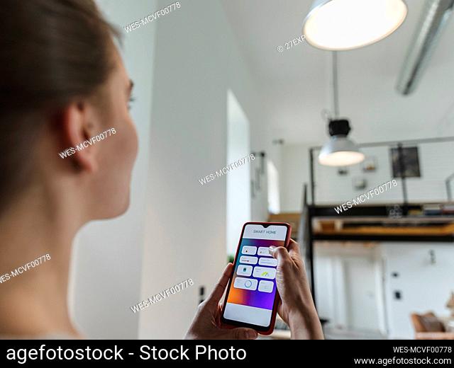 Young woman controlling light using mobile phone at home