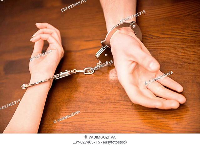 Hands of man and woman are wearing in handcuffs, on the table