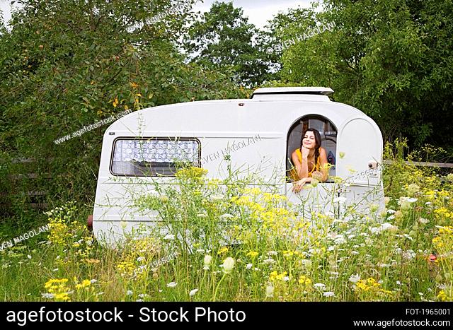 Young woman relaxing inside camper trailer in idyllic meadow