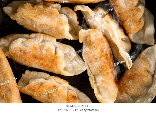 Close up cooking fried dumplings in a frying pan. Chinese dish with hot steams, on rustic vintage wooden background