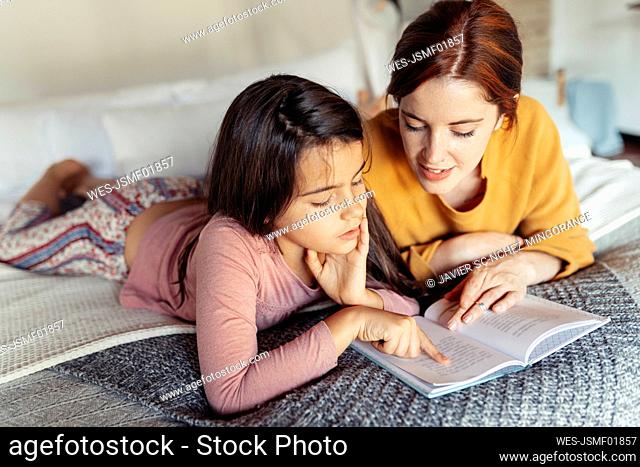 Girl and woman reading book while lying on bed at home