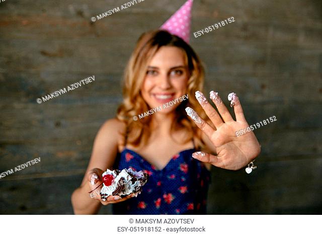 Beautiful funny girl in festive hat showing her palm in cream after eating a birthday cake
