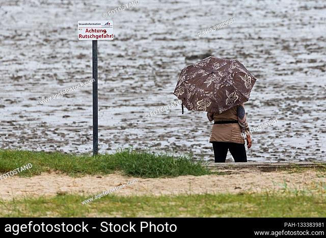 Harlesiel / Carolinensiel, Germany June 2020: Symbolic images - 2020 woman stands with umbrella on the beach of Harlesiel on the North Sea and looks at the sea