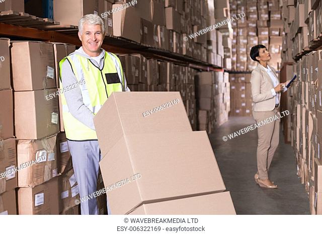 Warehouse worker moving boxes on trolley in a large warehouse