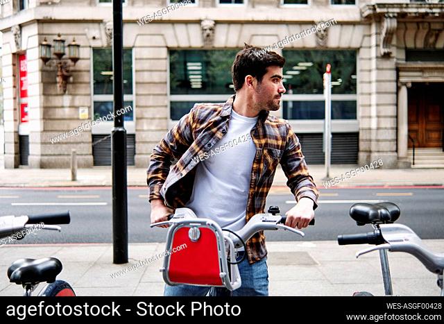 Young man looking away while sitting on bicycle on footpath