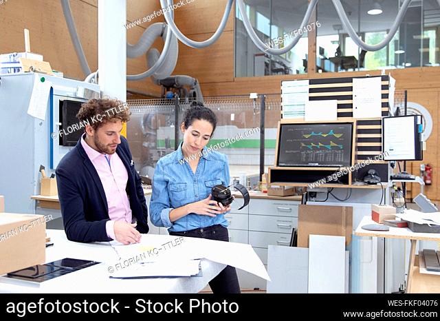 Male entrepreneur explaining strategy to female colleague holding ear protectors in factory