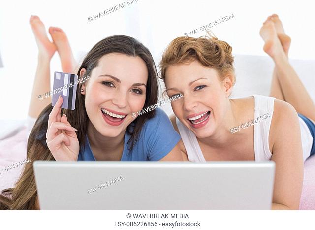 Cheerful relaxed friends doing online shopping in bed