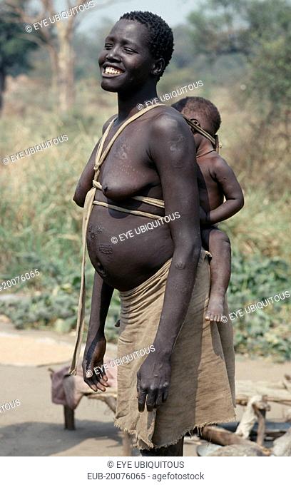 Uduk refugees from Sudan. Smiling pregnant woman carrying baby on her back in cloth and wood sling. Note scarification on stomach