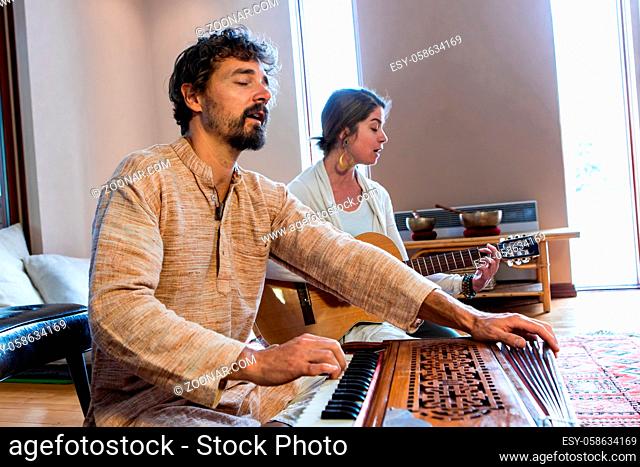 Senior man with woman playing musical instrument harmonium and classical guitar together as sacred and kirtan music for meditation and peace