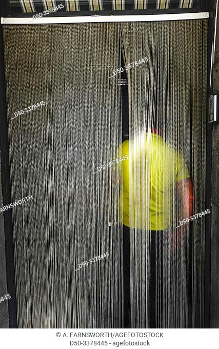 Syracuse, Sicily, Italy A man in a yellow shirt stands inside a cafe with hanging drapery. in the doorway