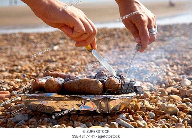 Young person barbequing sausages on the beach