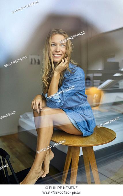 Smiling young woman sitting on table behind windowpane