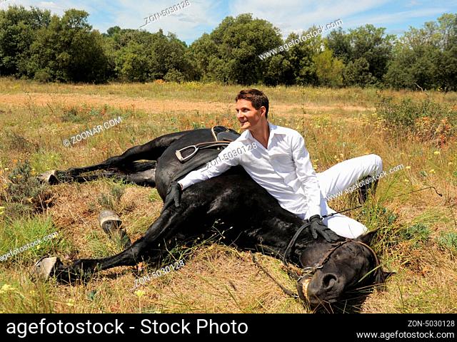 young man and his black stallion in a field