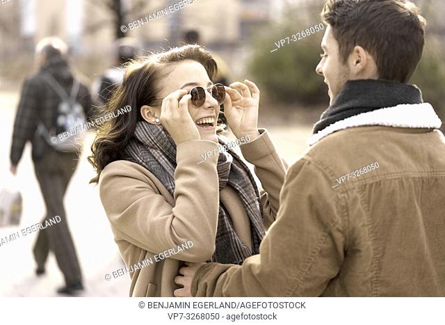 enthusiastic teenage woman touching sunglasses while looking at boyfriend, in Cottbus, Brandenburg, Germany