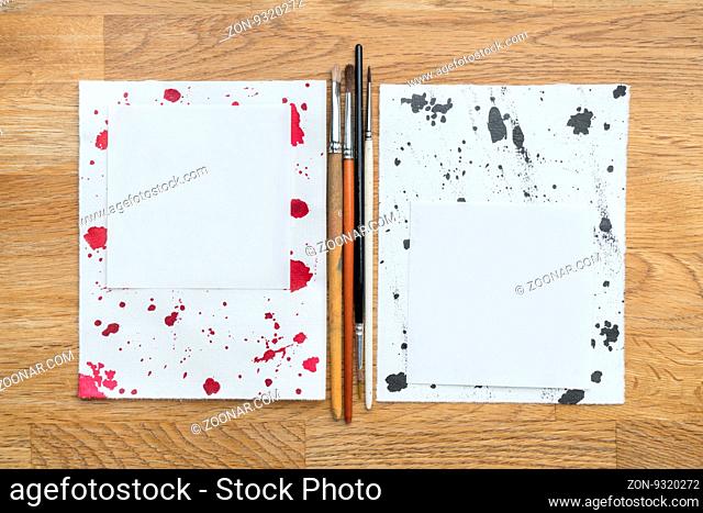 Two piece of papers spotted with ink and brushes in a wooden background