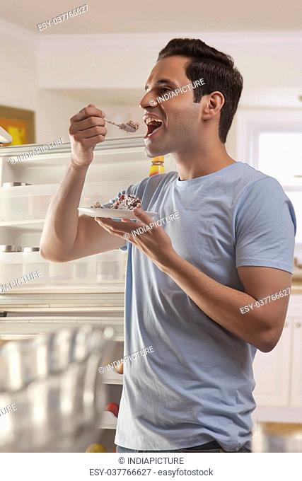 Young man standing in front of open refrigerator eating pastry