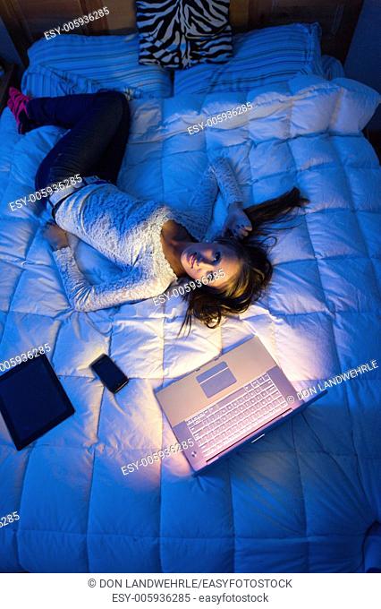 Teenage girl lying on a bed at night with a laptop computer