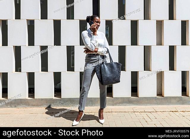 Mid adult businesswoman with purse talking on mobile phone during sunny day