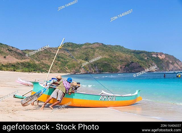 Kuta, Lombok, Indonesia - July 16, 2015: Two fisherman on the beach are pushing a fishing boat into the ocean to go fishing