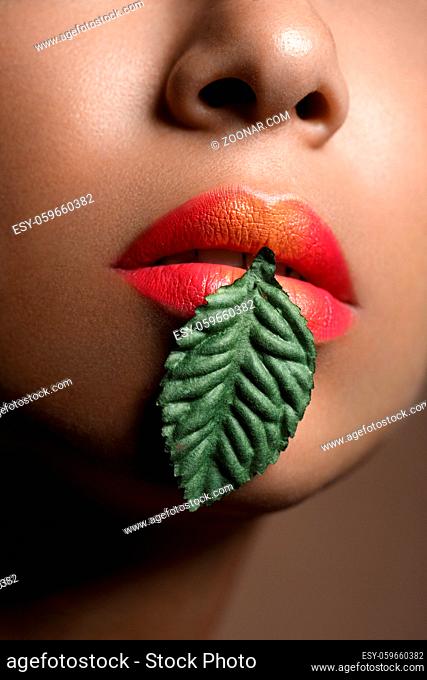 closeup shot of full sexy woman lips with orange lipstick. plant leaf in mouth. copyspace