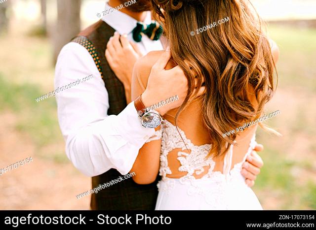 Groom hugs the shoulders of bride in a beautiful embroidered white dress. Bride stands with her back turned. High quality photo