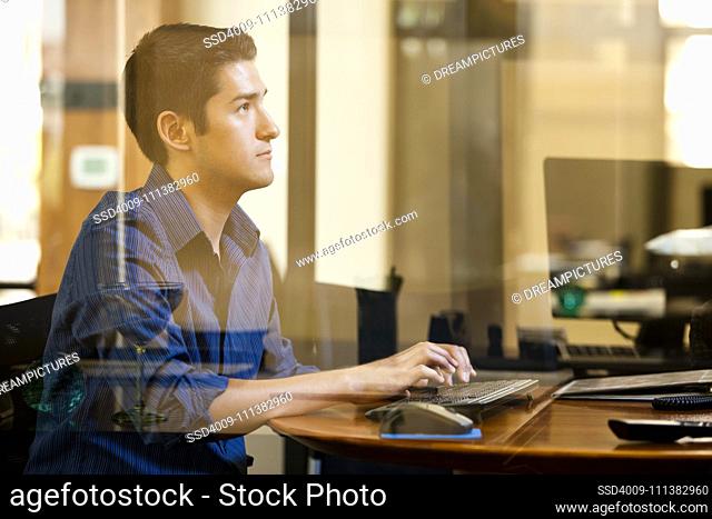 Hispanic man using computer behind glass