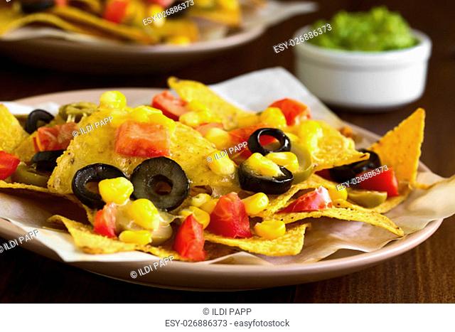 Baked nachos with cheese, green and black olives, tomato and corn, photographed with natural light (Selective Focus, Focus one third into the nachos)