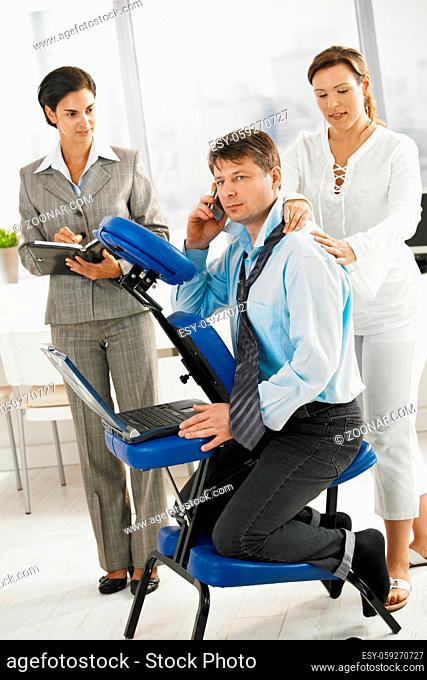 Businessman talking on mobile while getting neck massage in office