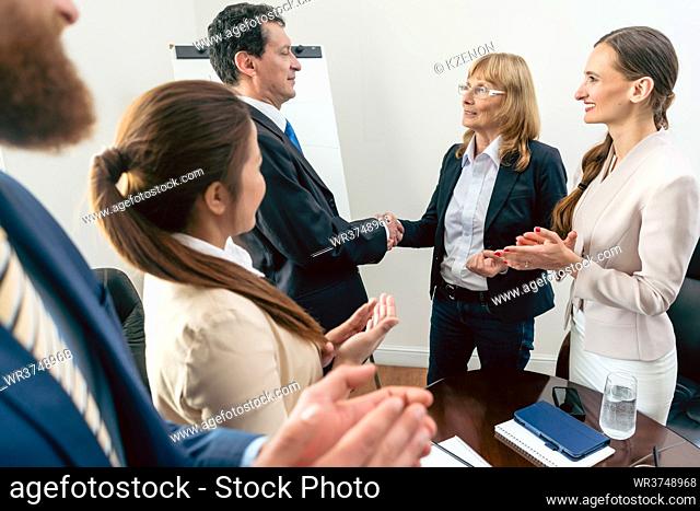 Two middle-aged business associates smiling while shaking hands as agreement after meeting in the conference room of a multinational company