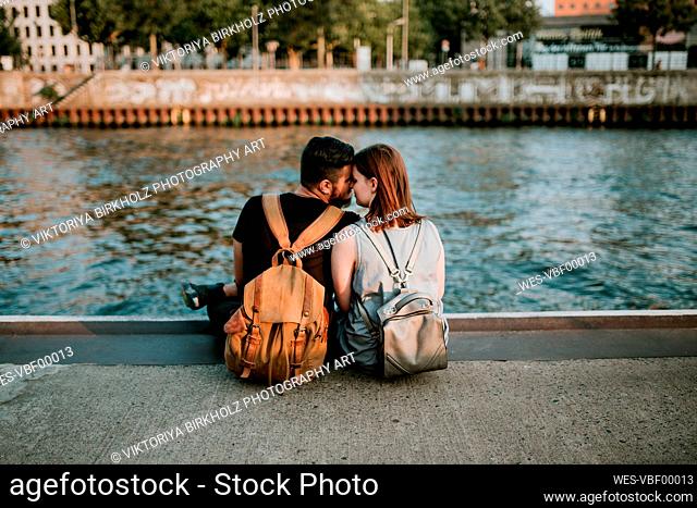 Affectionate young couple sitting at River Spree, Berlin, Germany