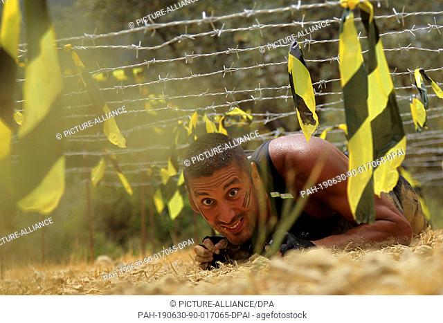 30 June 2019, Lebanon, Batroun: A participant crawls under barbed wires during the 6th Puma Hannibal Race, an annual 8-kilometer obstacle race at Zen Batroun...