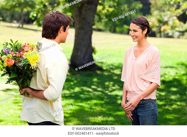 Woman smiling as she greets her friend who is holding flowers behind his back