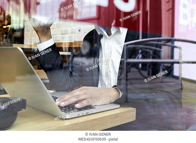 Senior businessman behind windowpane in a coffee shop working on laptop