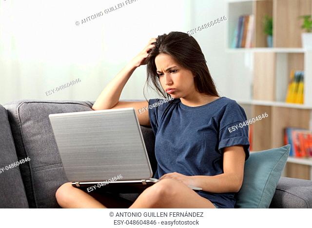 Confused teen reading online content sitting on a couch in the living room at home