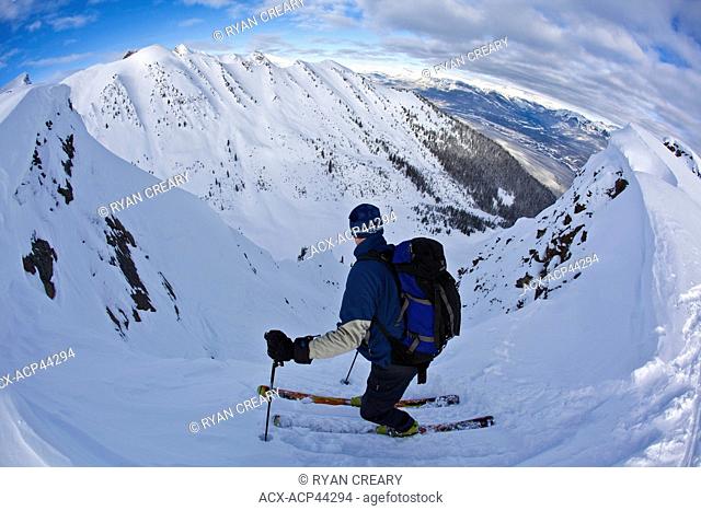 A middle aged man contemplates before dropping into a steep chute , Kicking Horse Backcountry, Golden, Britsh Columbia, Canada