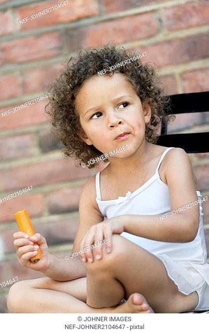 Girl eating carrot outside building