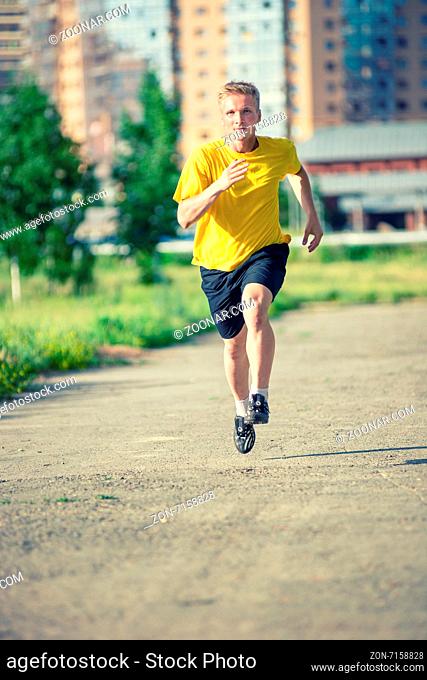 Running man jogging in city street park at beautiful summer day. Sport fitness model caucasian ethnicity training outdoor