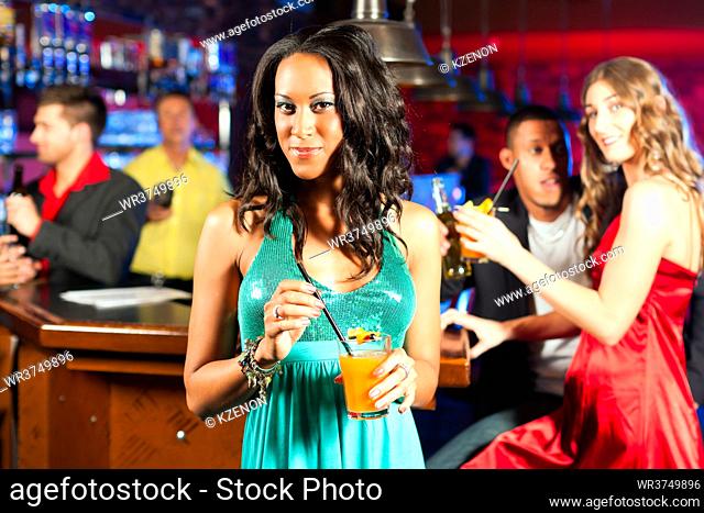 Group of party people with cocktails in a bar or club having fun; one woman is looking into the camera