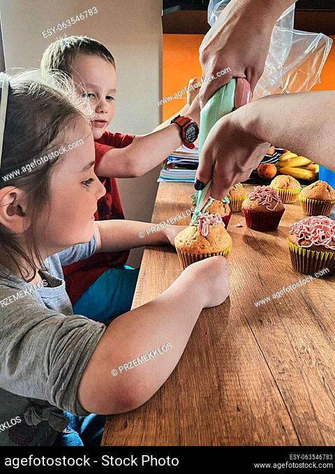 Group of children baking cupcakes, squeezing cream from confectionery bag, preparing ingredients, topping, sprinkles for decorating cookies