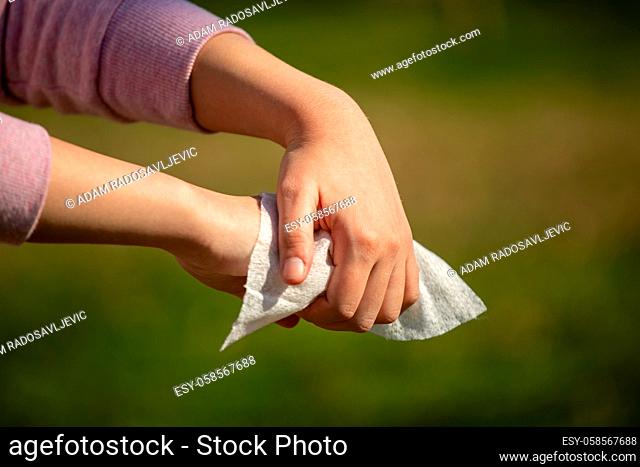 Cleaning hands with wet wipes outdoor against disease infection versus flu or infulenza, blurred green background