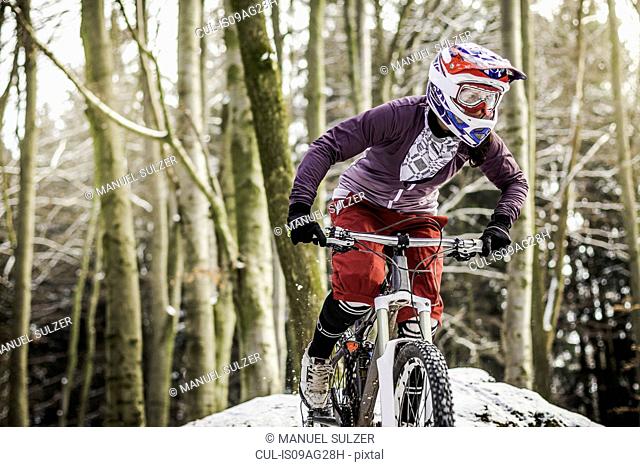 Young female mountain biker riding through forest
