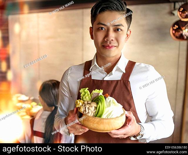 young waiter bring vegetables for hot pot and serving customer in restaurant