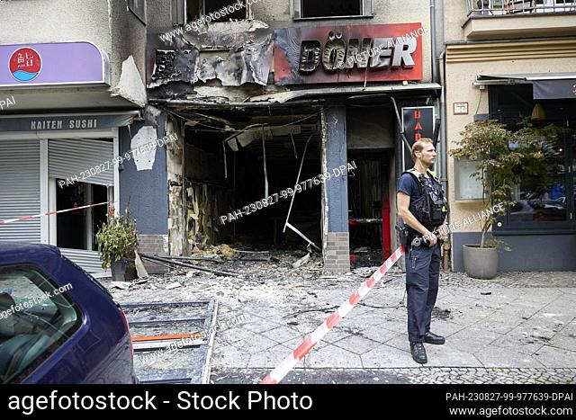 27 August 2023, Berlin: A policeman stands in front of a burnt-out kebab restaurant in Uhlandstraße. According to the police spokesman
