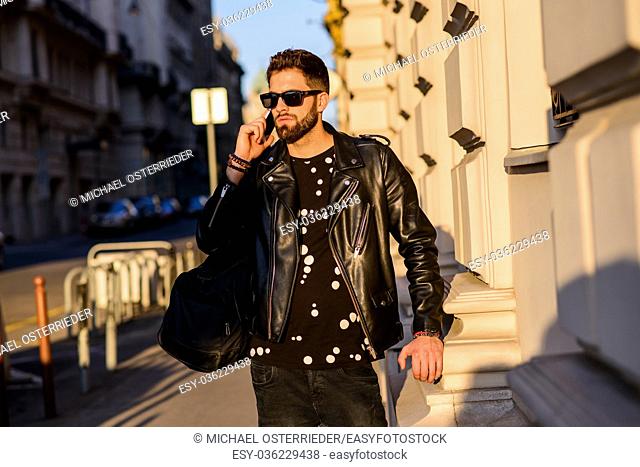 A handsome young hipster man walking on a sunny street while talking on his smartphone