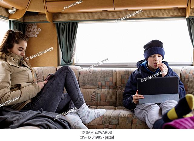 Teenage brother and sister using digital tablet and smart phone in motor home